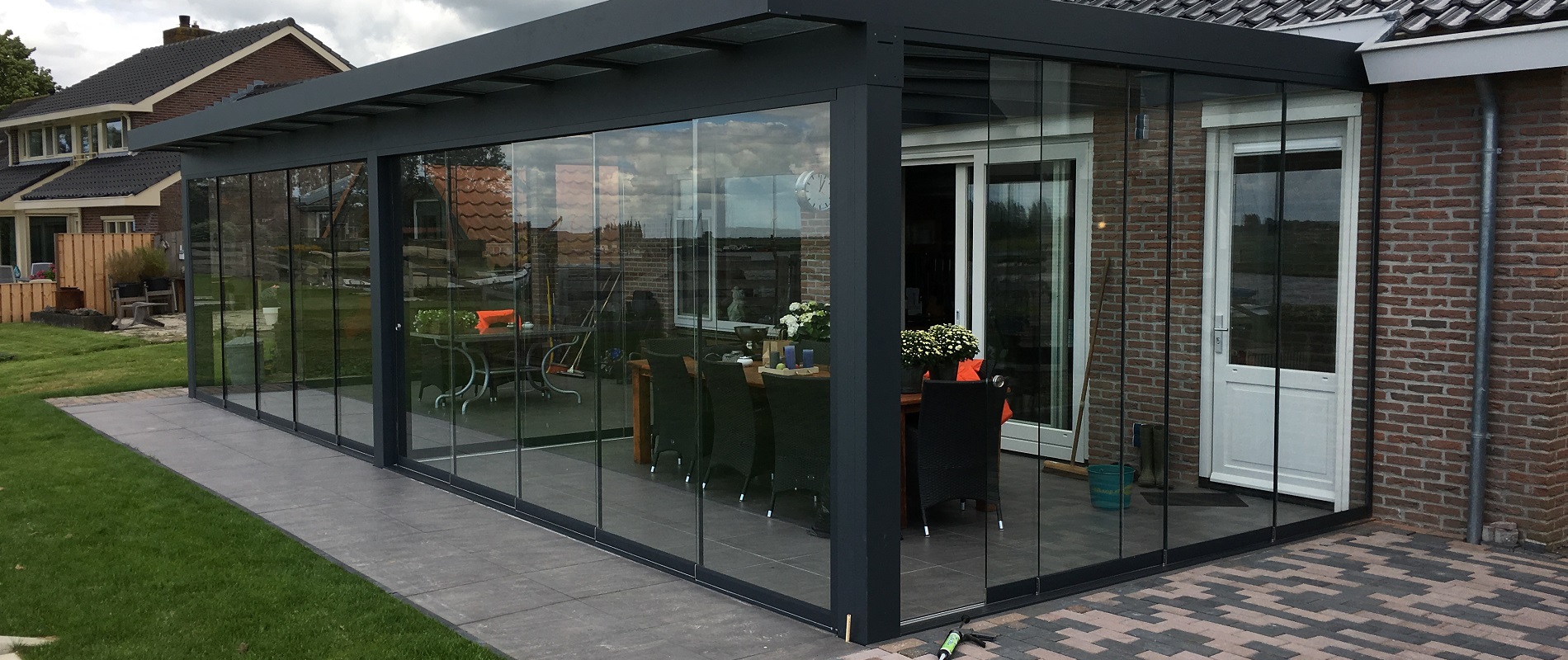 Een moderne tuinkamer met aluminium frame en glazen wanden, omringd door weelderige natuur en biedt een adembenemend uitzicht op de buitenwereld.